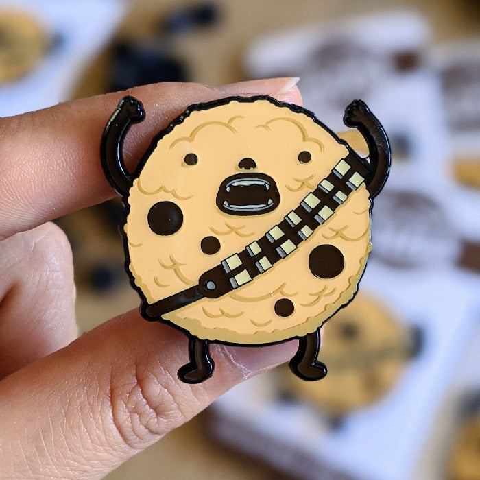 lapel pin that looks like a cookie but also chewie from star wars! he has his arms above his head. over white background.