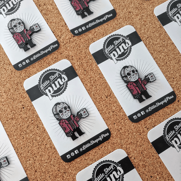 multiple I heart Friday Jason Enamel Pins on backing cards on a cork board.